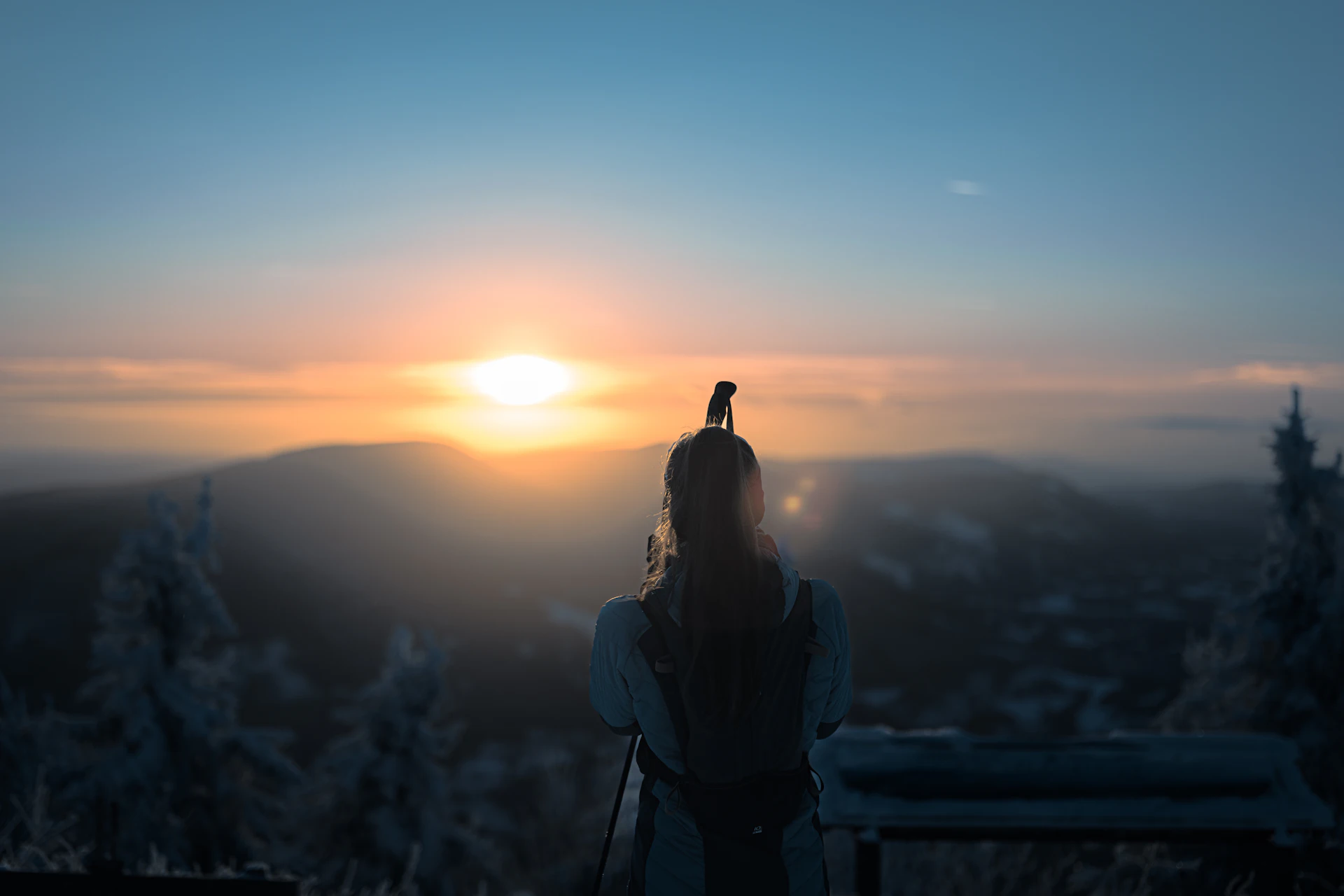 A woman watching the sun rise over snowy hills