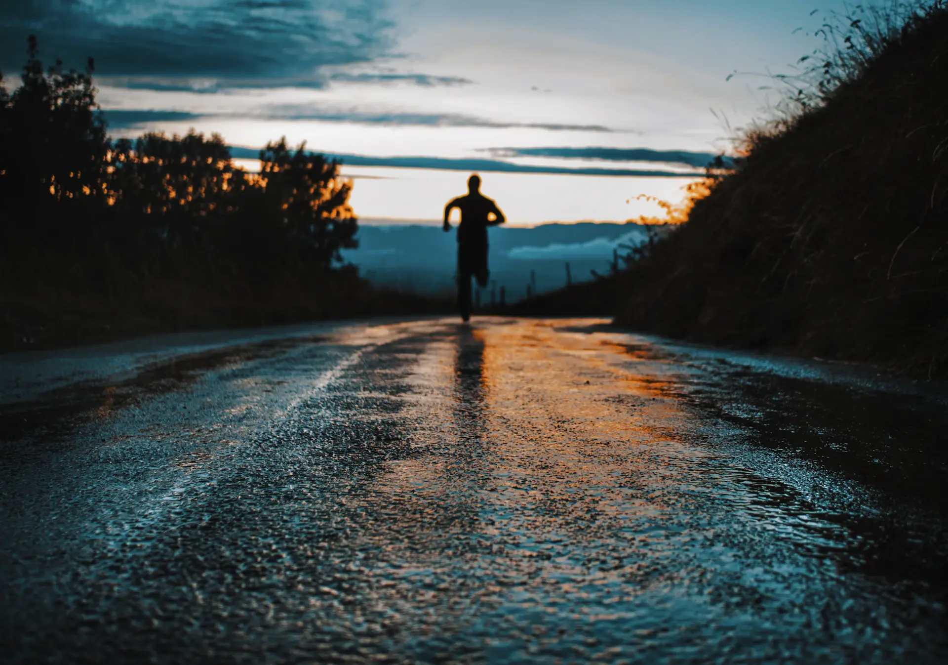 A runner heading down a wet country road at dusk