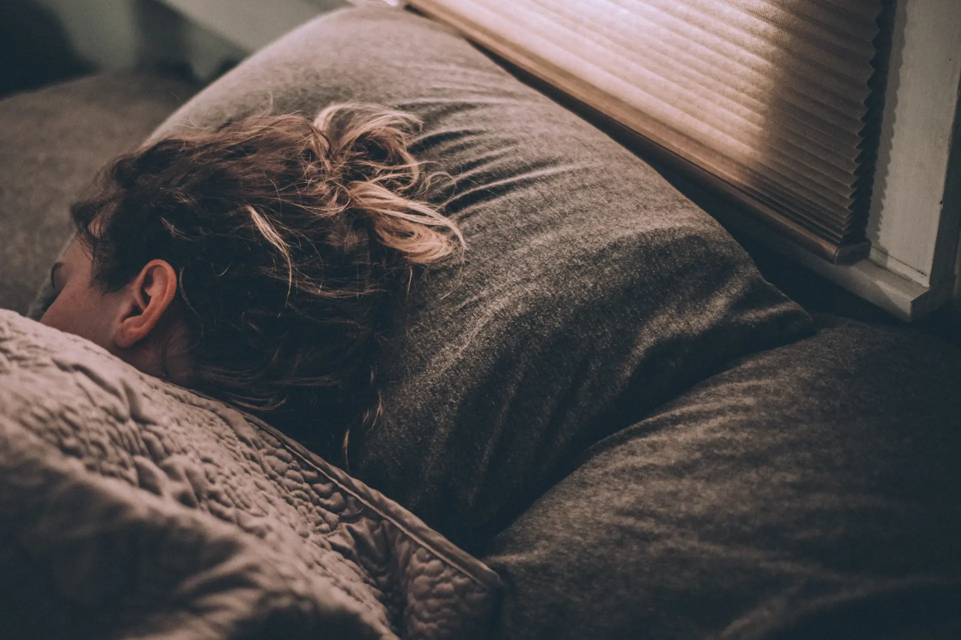 A woman asleep under a heavy blanket in soft evening light