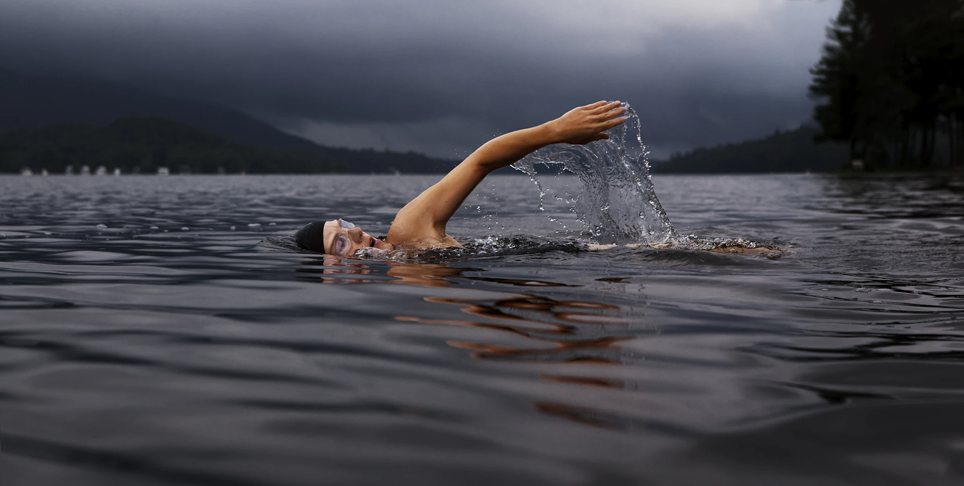 A swimmer mid-stroke in open water under a dark, cloudy sky