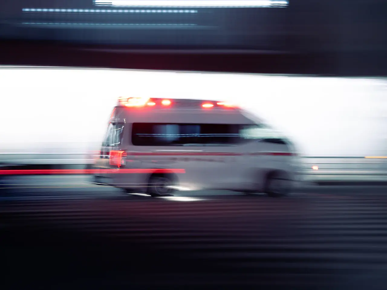 An ambulance with its lights on, moving at night