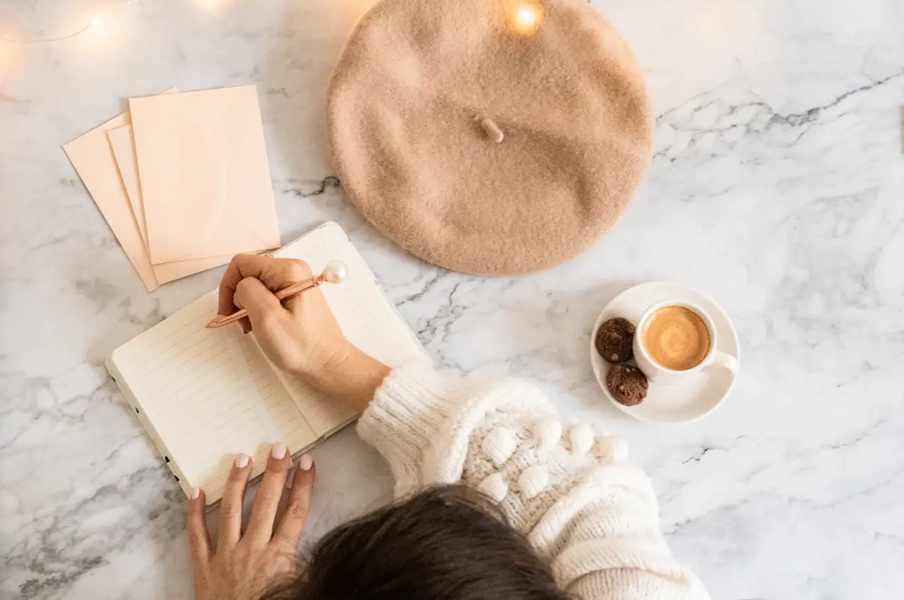 Someone writing in a journal next to a cup of coffee