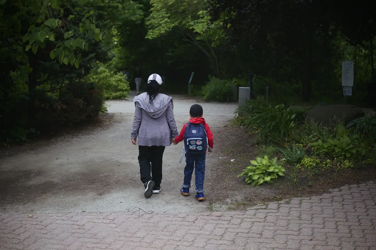 A mother and child walking hand in hand along a park path