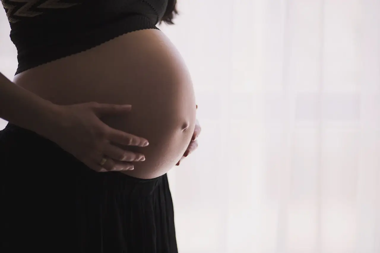 A pregnant woman cradling her belly in soft window light