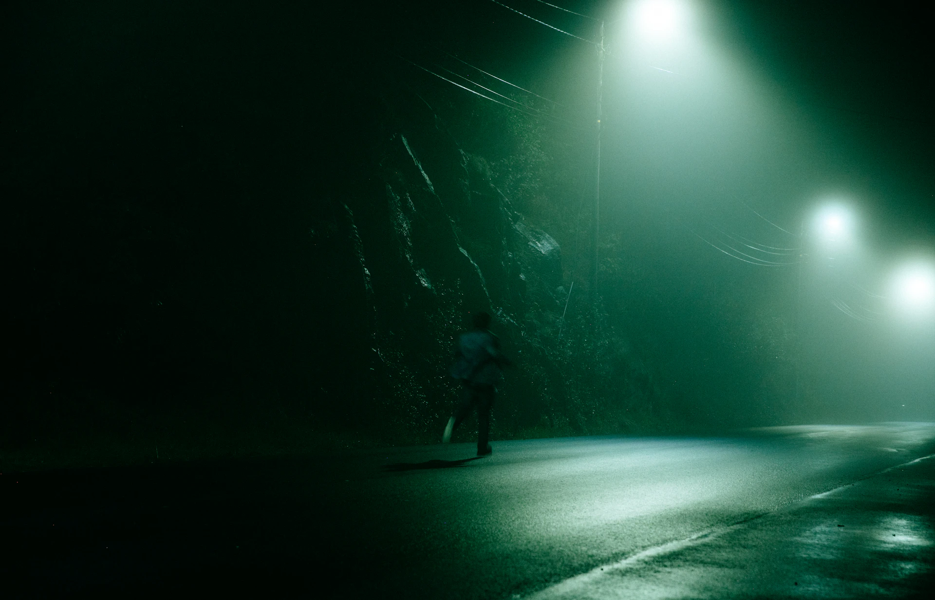 A runner on a misty road at night under green-tinted street lights